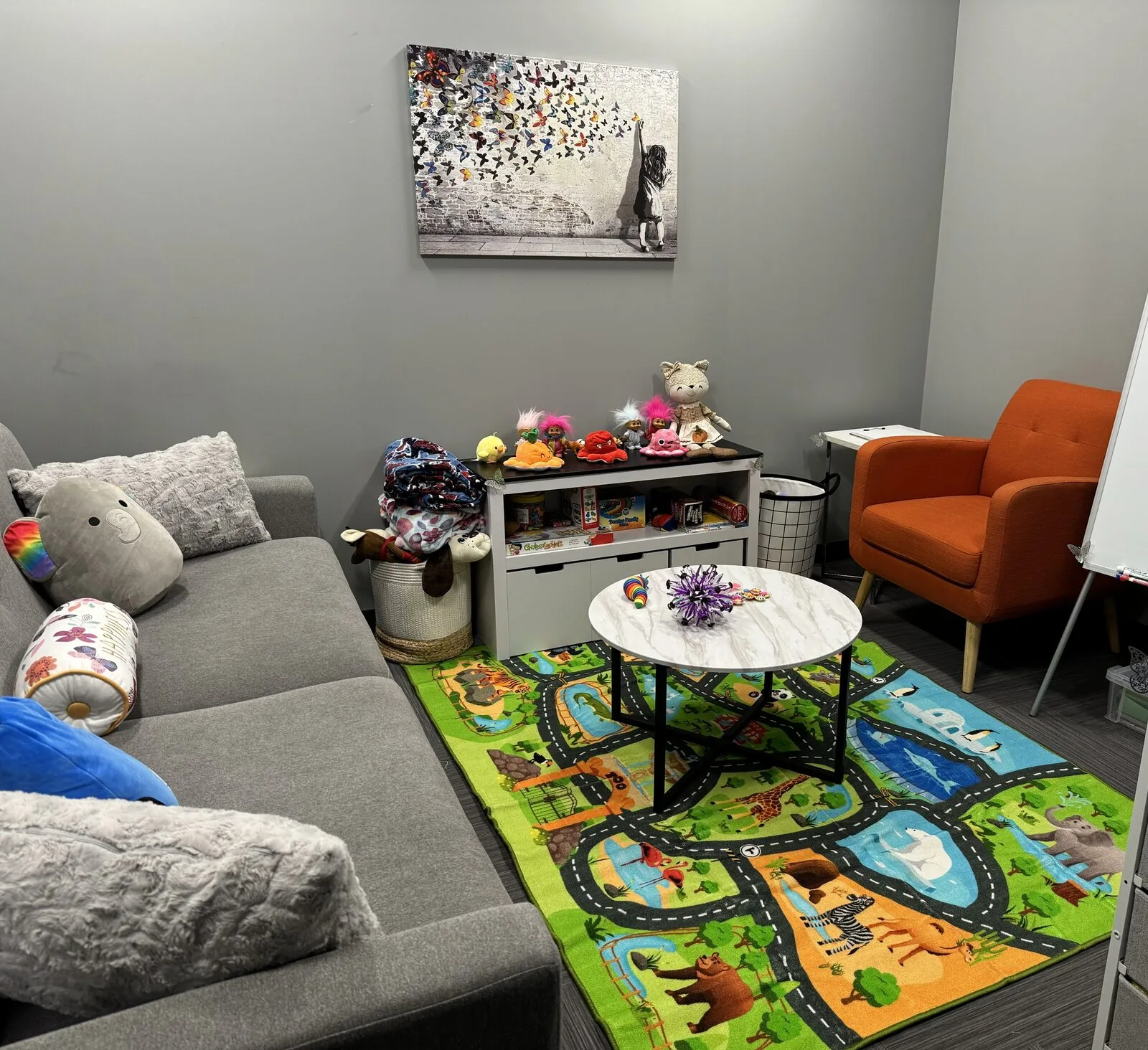 The bright, child-friendly play therapy room at the Flutterby Psychology office, with a soft couch, toys, and a colourful play mat